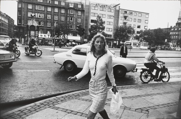 Untitled (Woman in long sleeved white shirt with plaid skirt, walking in front of a white car)